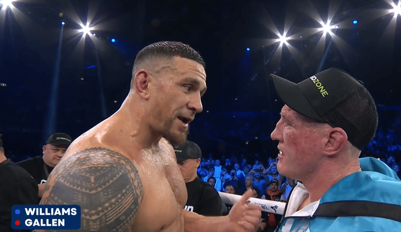 A head-and-shoulders shot of two male boxers, one shirtless and heavily tattooed on his left arm, and the other wearing a black cap with DAZONE in yellow text and a light blue or teal jacket. They are looking at each other and appear to be talking. The background is a brightly lit arena with a crowd visible. Text overlays in the bottom left corner read WILLIAMS in blue next to a blue circle, and GALLEN in red next to a red circle.