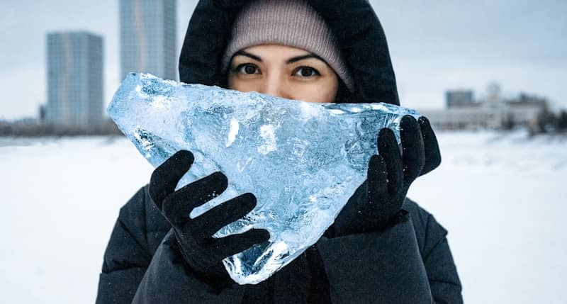 A woman holding a piece of ice in front of her face