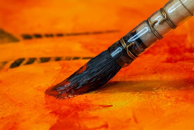 A paintbrush applies orange paint to a textured surface.
