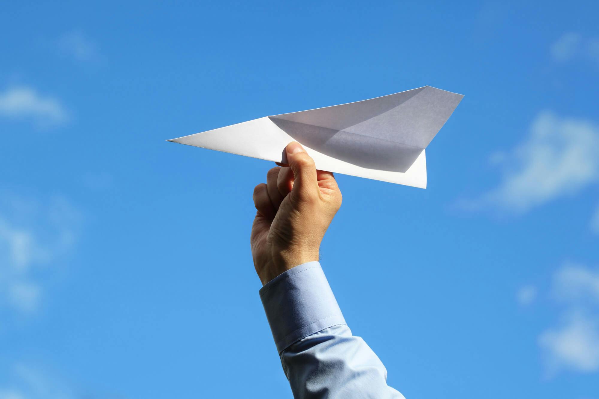 Hand holding paper airplane against blue sky