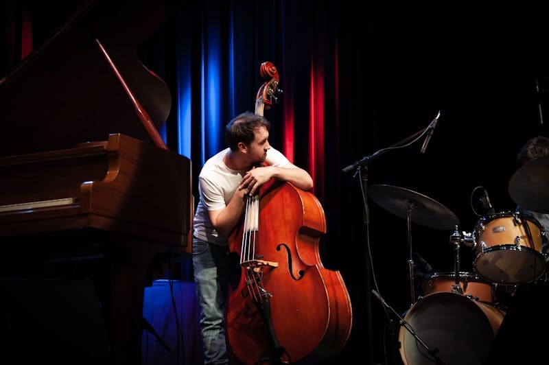 a man holding a cello while standing next to a piano