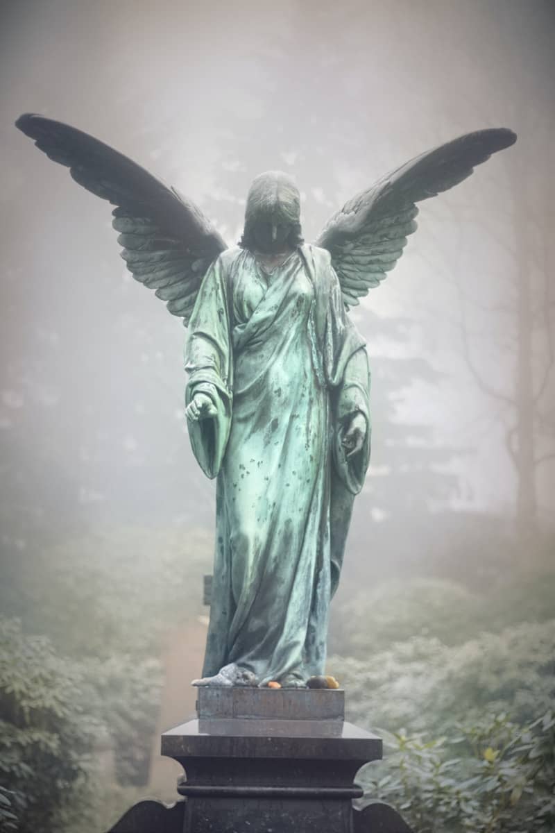 Angel statue with wings spread in foggy cemetery