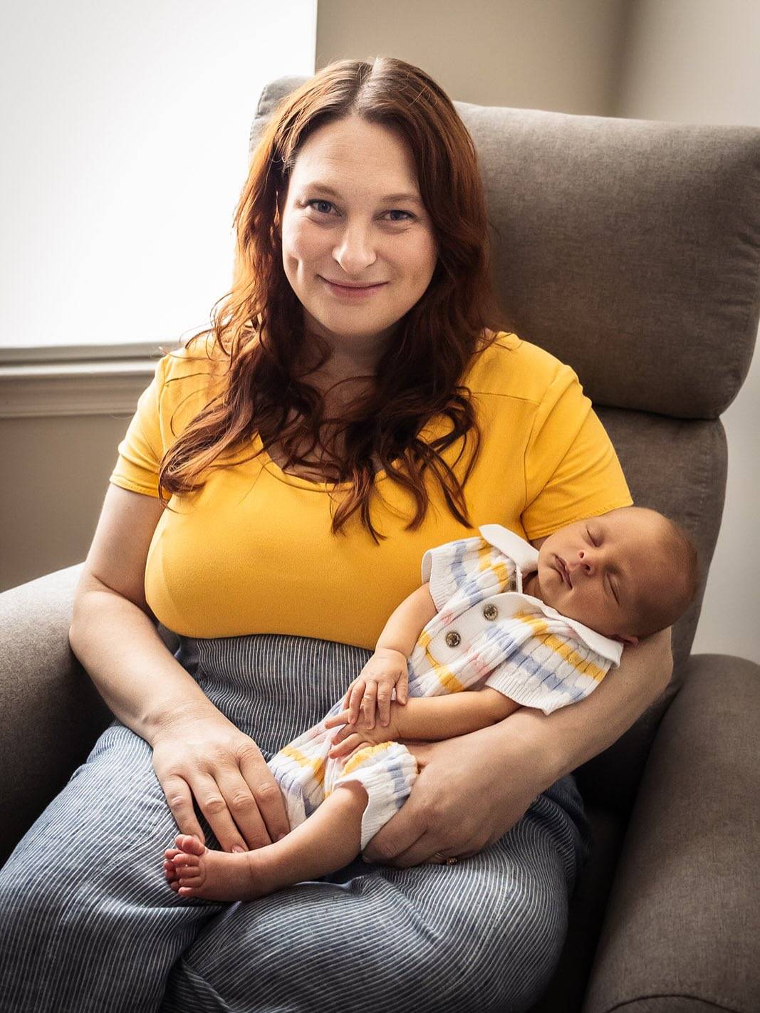 a woman with long red hair and a yellow top holds a newborn baby