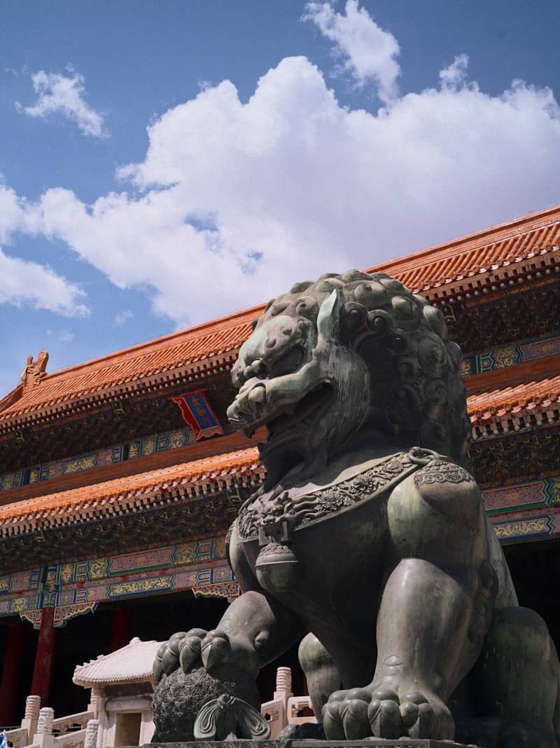 Bronze lion statue guards ornate building under blue sky