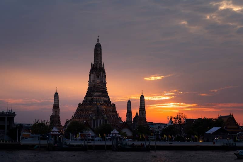 Wat arun temple silhouetted against a vibrant sunset sky.