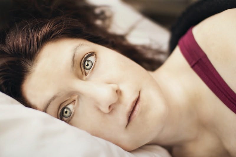 Young woman lies in bed, haunting eyes wide open following a night of insomnia, and ponders what today will bring - more of the same exhaustion, depression and sadness following the separation from her husband?