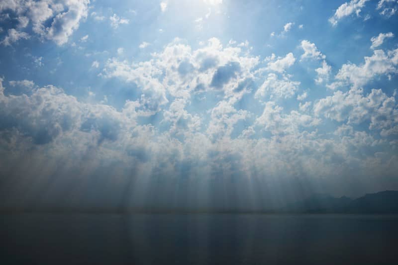 Sunlight streaming through clouds over a calm dark sea with distant mountains