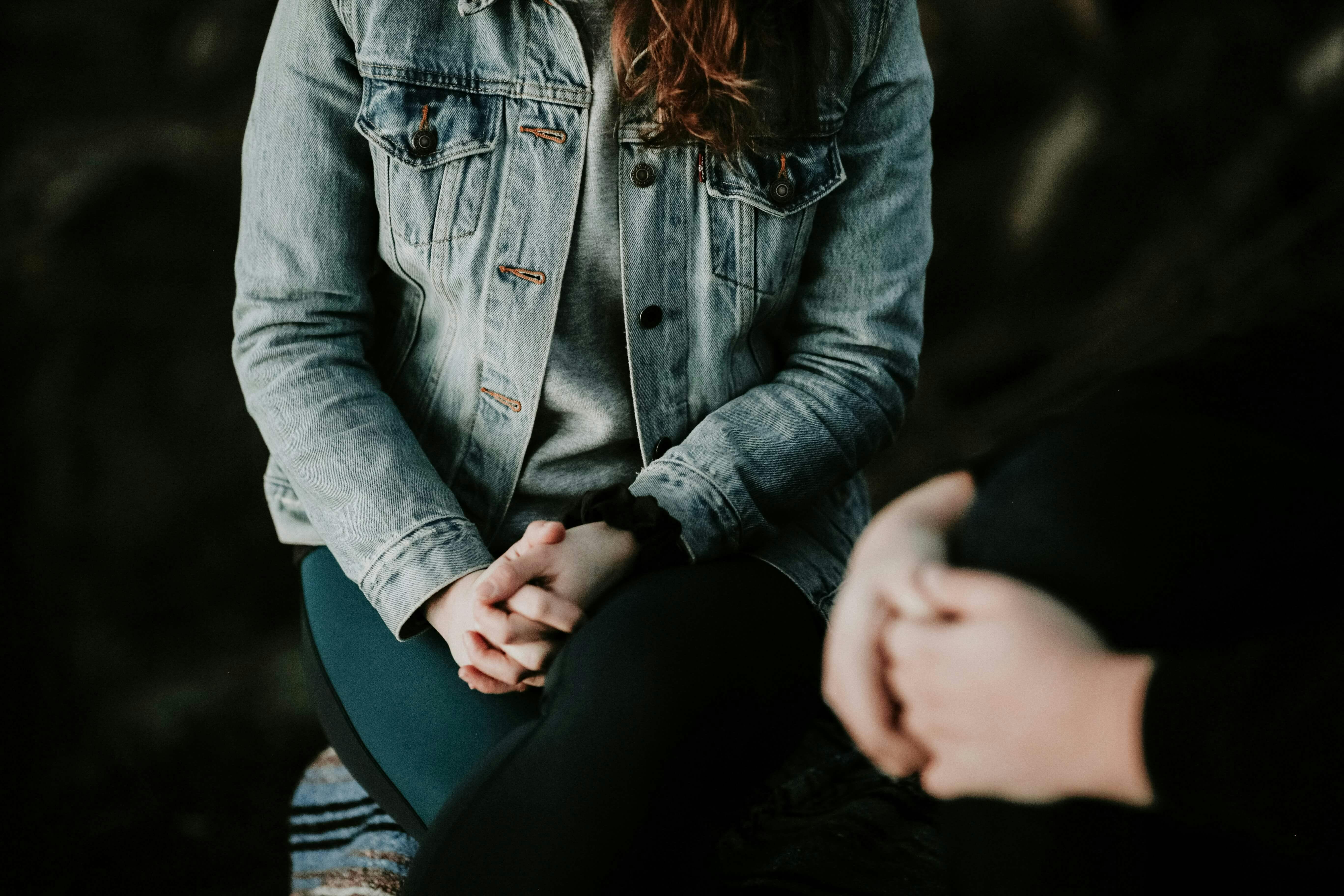 The torsos of two people are in screen, with their hands folded in front of them, angling toward each other as if in a deep conversation.