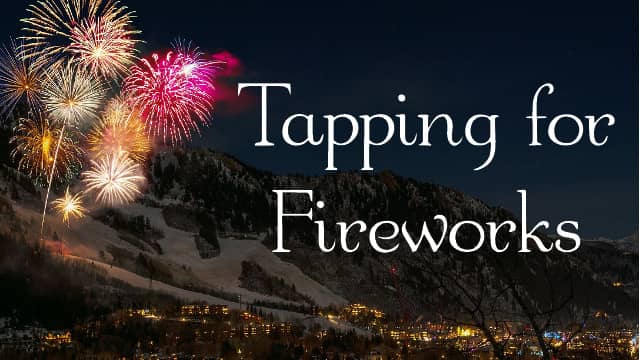 Fireworks over a mountain landscape with a stown at the base of the mountain.