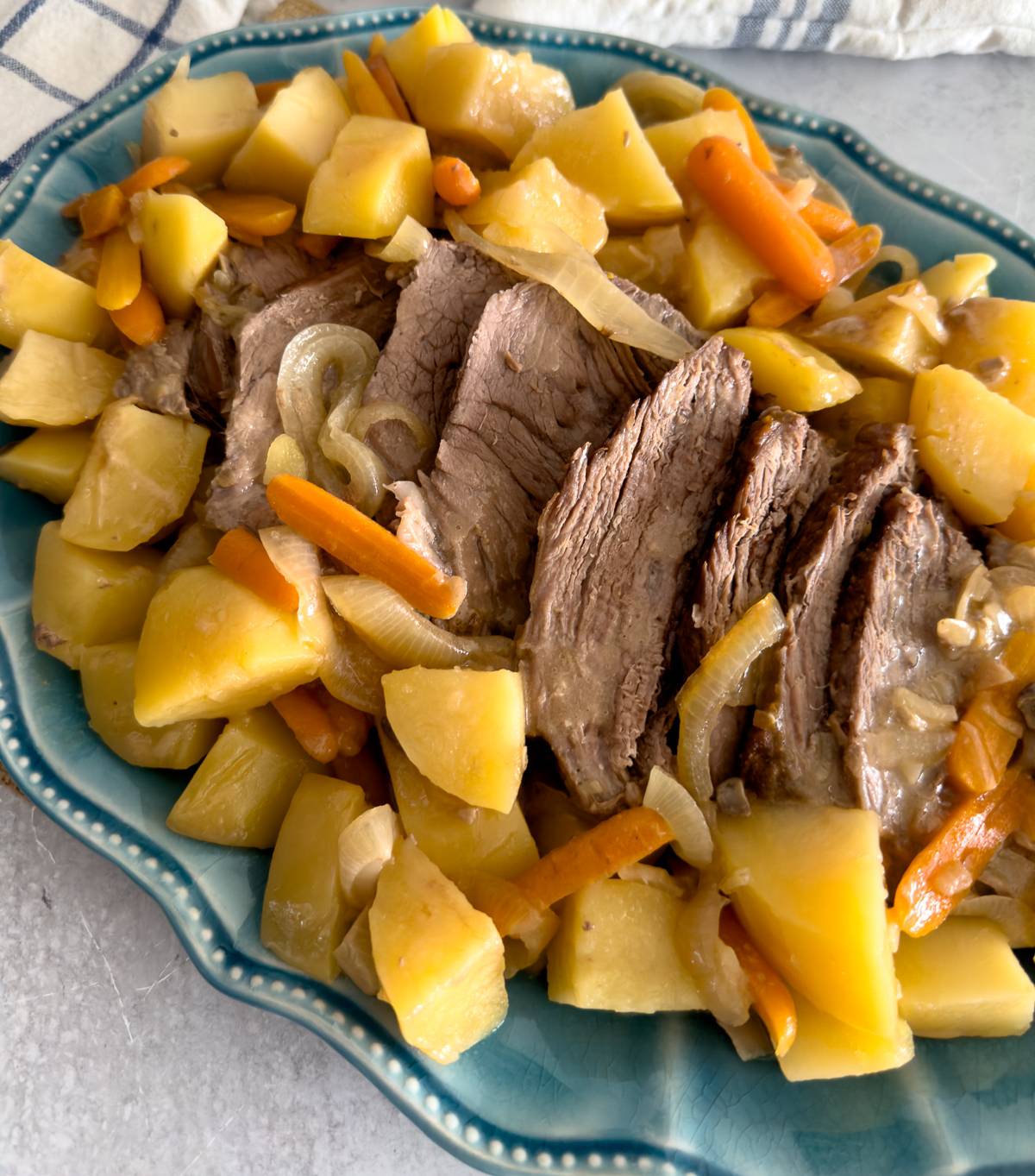 tender chuck roast nestled on a blue serving platter with onions, potatoes, and carrots