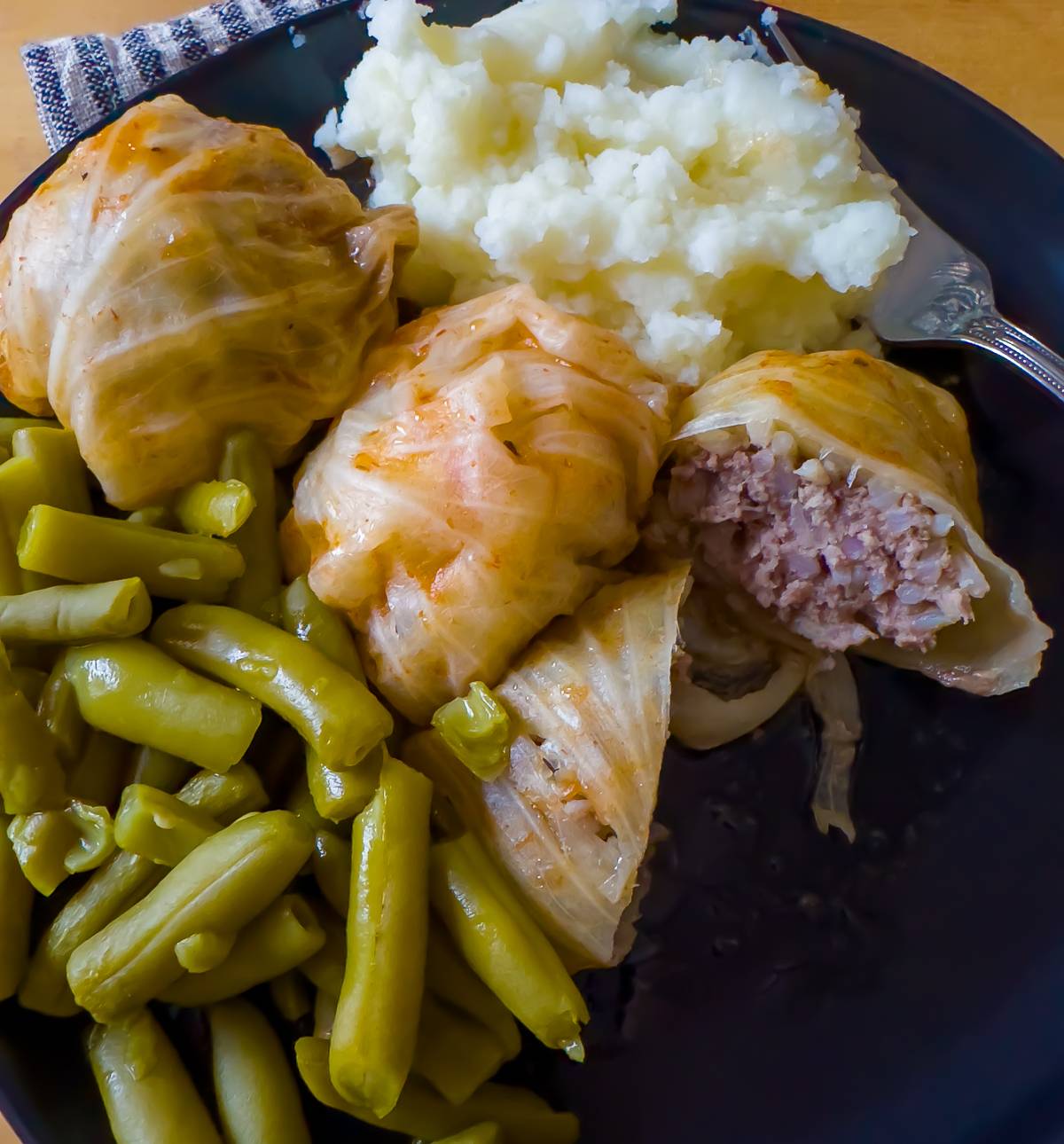 Overhead view of a dinner plate with stuffed cabbage rolls, green beans, and homemade mashed potatoes. 