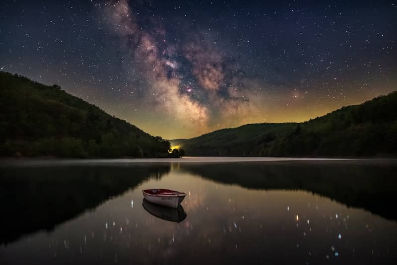Milky way shines above a tranquil lake at night.
