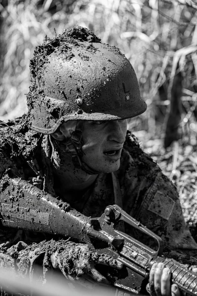 Soldier covered in mud crawls with rifle.