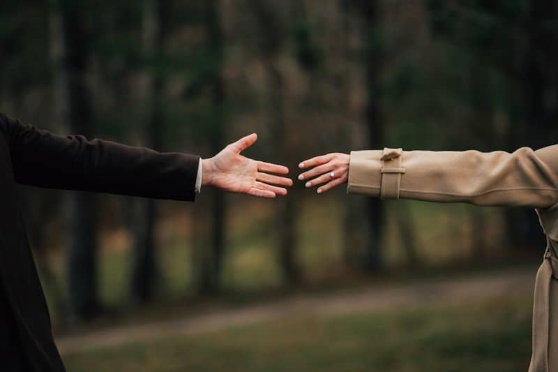 Two people reaching toward each other in a dark coat and beige trench coat