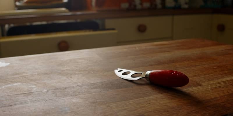 A cheese knife rests on a wooden table.