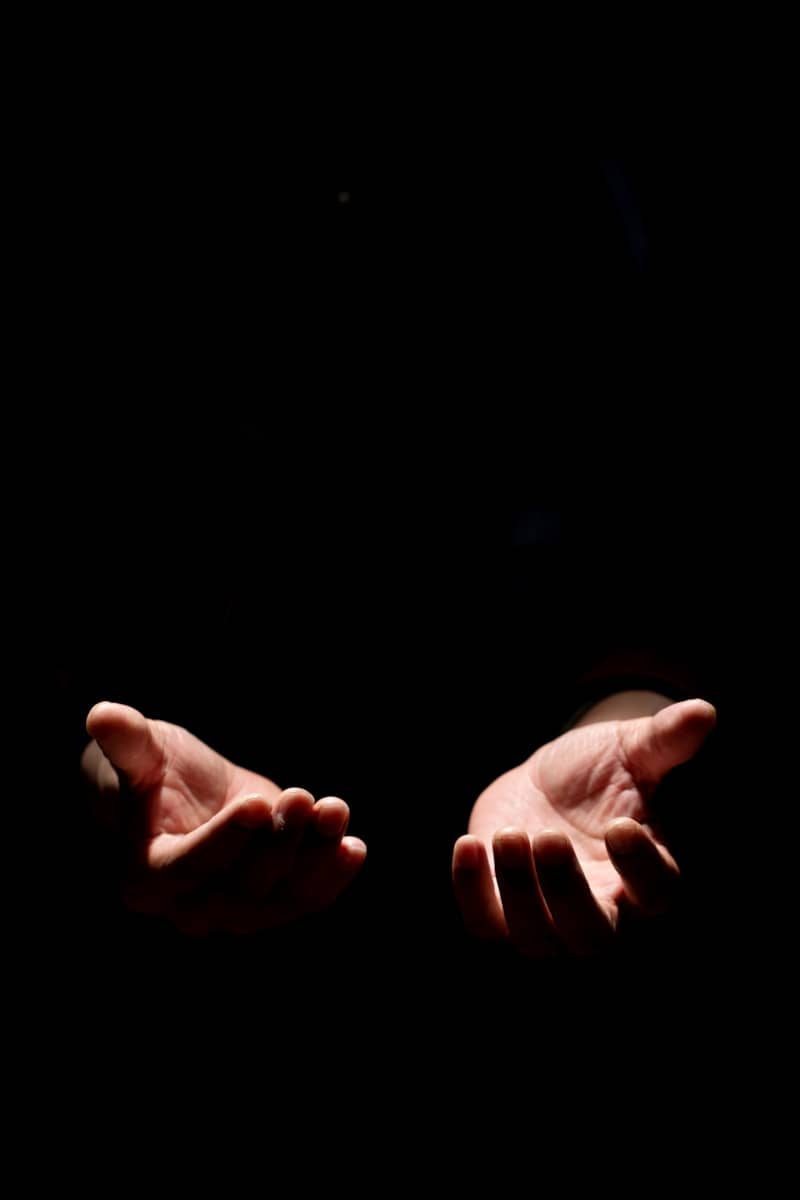 Two open hands reaching up from darkness