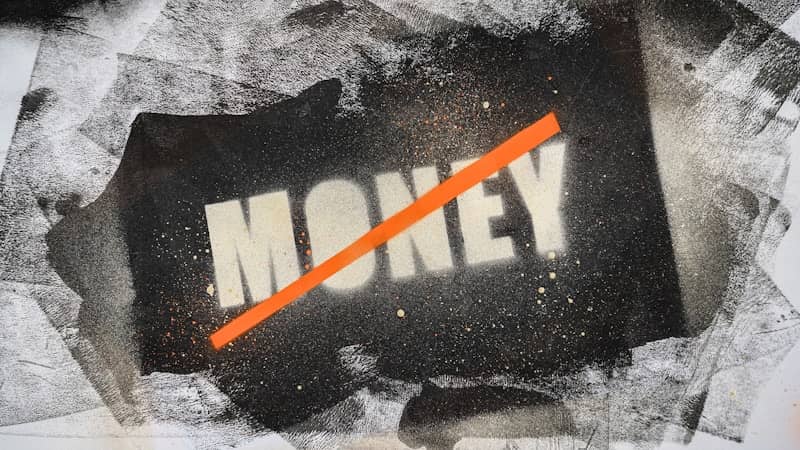 The word MONEY stenciled in white with an orange diagonal line across it