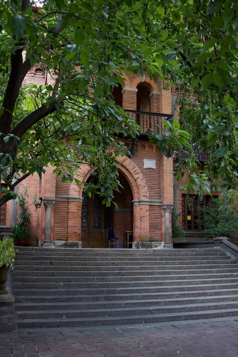 Brick building entrance framed by lush greenery.