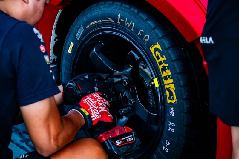 Mechanic tightening a wheel on a red car.