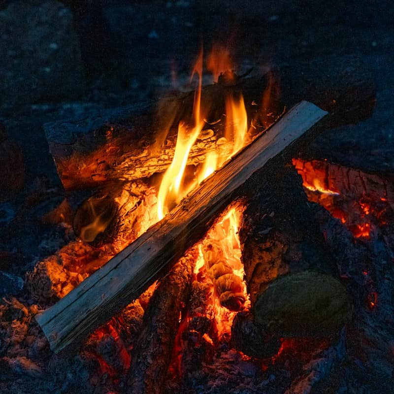 A bright campfire with orange flames licking at stacked wooden logs at night