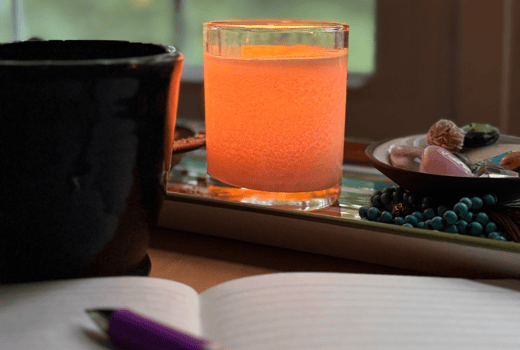 Lit candle on desk with mug and journal in front of it. 