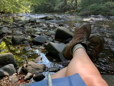 Legs propped up on rocks by river in the woods. 