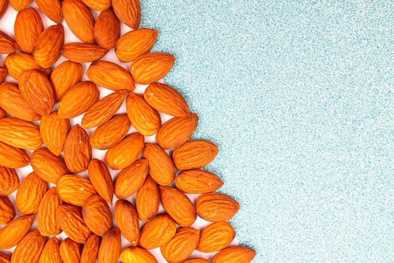 A pile of almonds on a textured blue background.