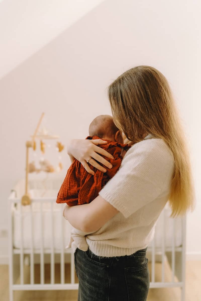 Mother holding her newborn baby near a crib