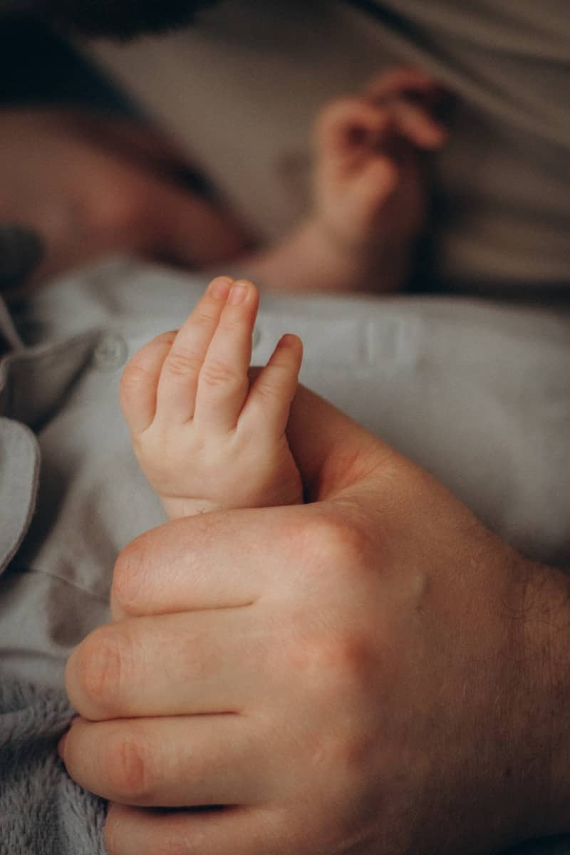 A baby's hand gripping an adult's finger.