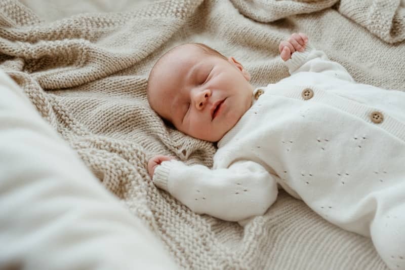 A newborn baby sleeps peacefully on a soft blanket.