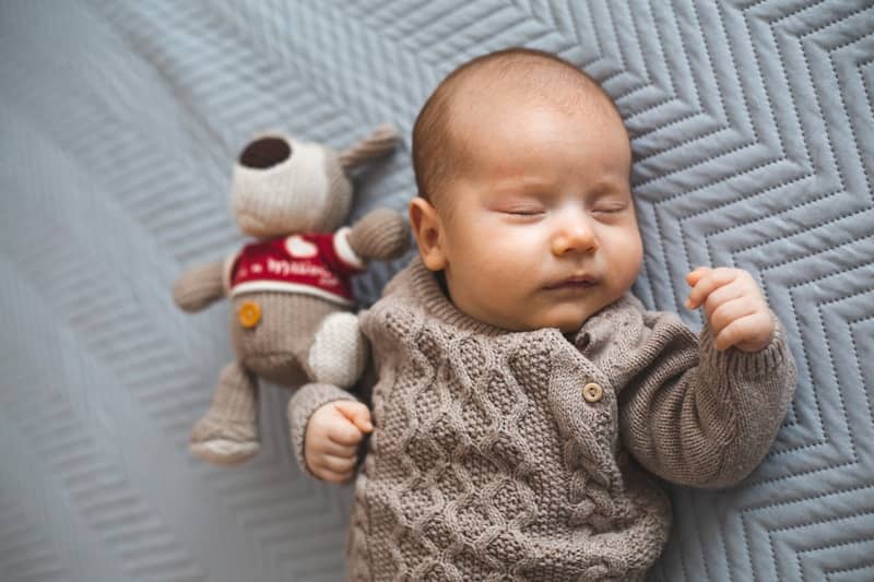 A baby sleeps peacefully next to a stuffed toy.