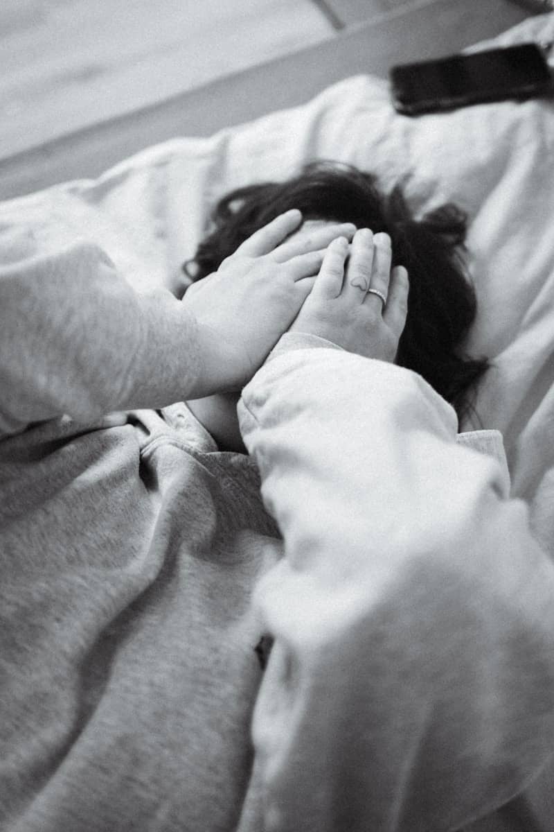Child covers face with hands while lying in bed.