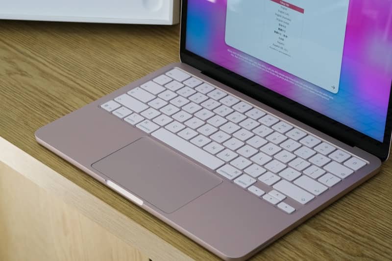 Rose gold laptop with white keyboard on a wooden desk.