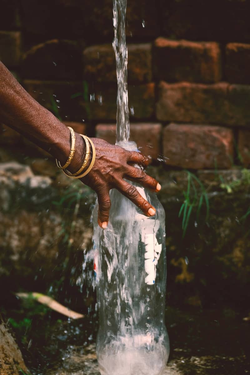 a person's hand is pouring water into a glass bottle