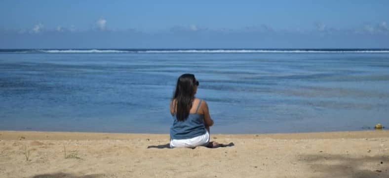 A woman sits on a beach looking at the ocean.
