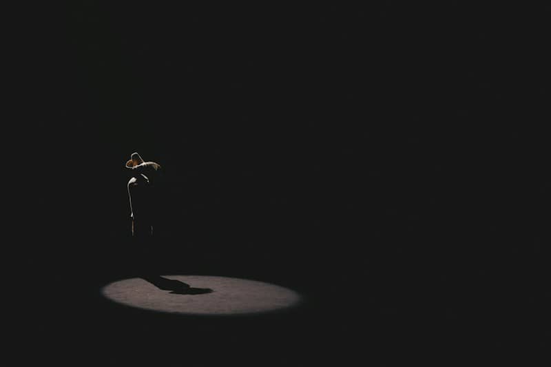 A person in a cowboy hat standing in a bright spotlight against darkness