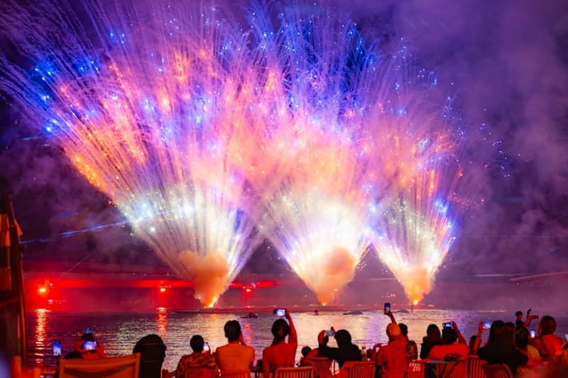 Spectacular fireworks display over water with silhouetted crowd.