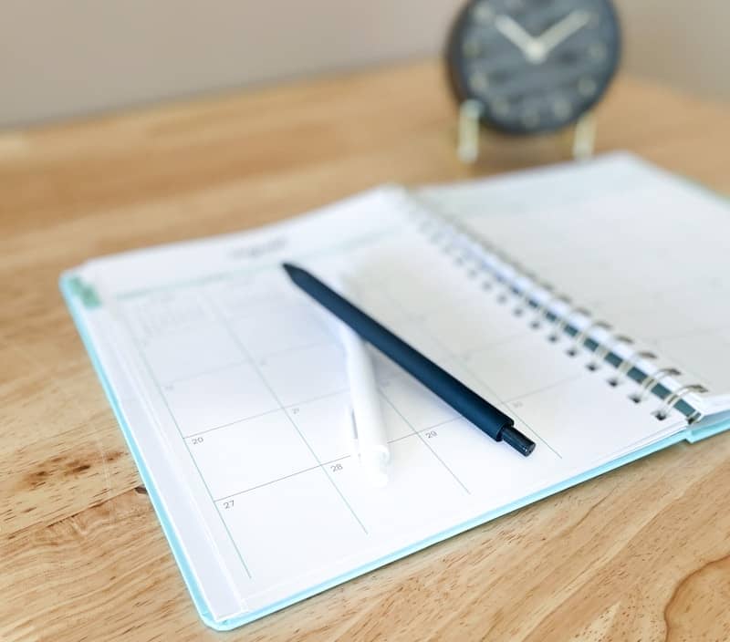 An open planner with a pen on a wooden desk.
