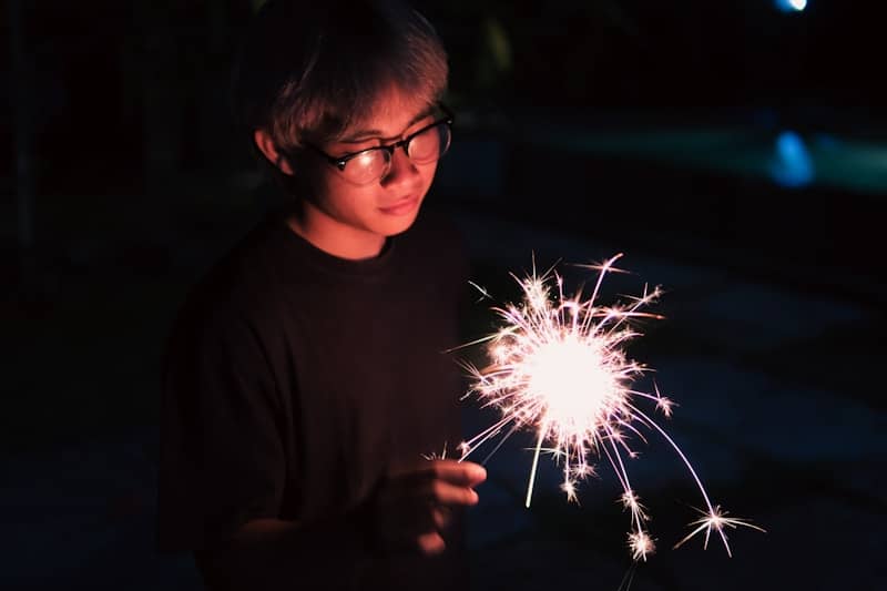 Young person holding a sparkling firework at night.