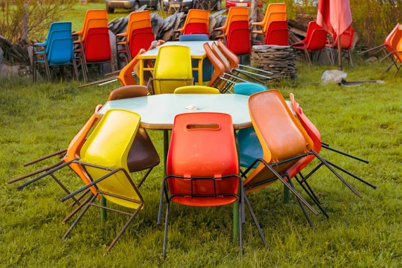 Colorful chairs stacked on tables in grassy outdoor setting