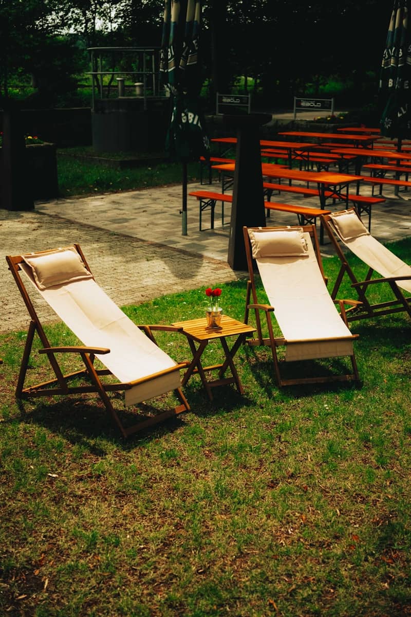 Beige lounge chairs and a small table on green grass.