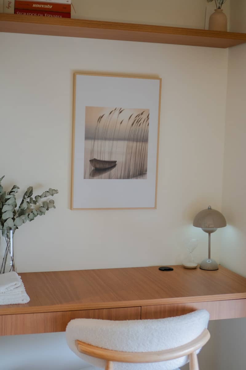 Wooden desk with framed artwork, chair, lamp, and vase.