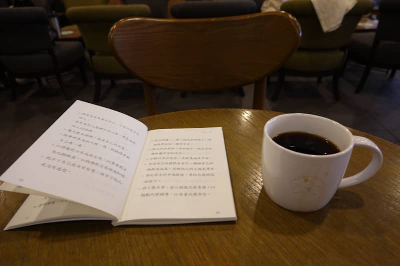 A white mug of coffee next to an open book.