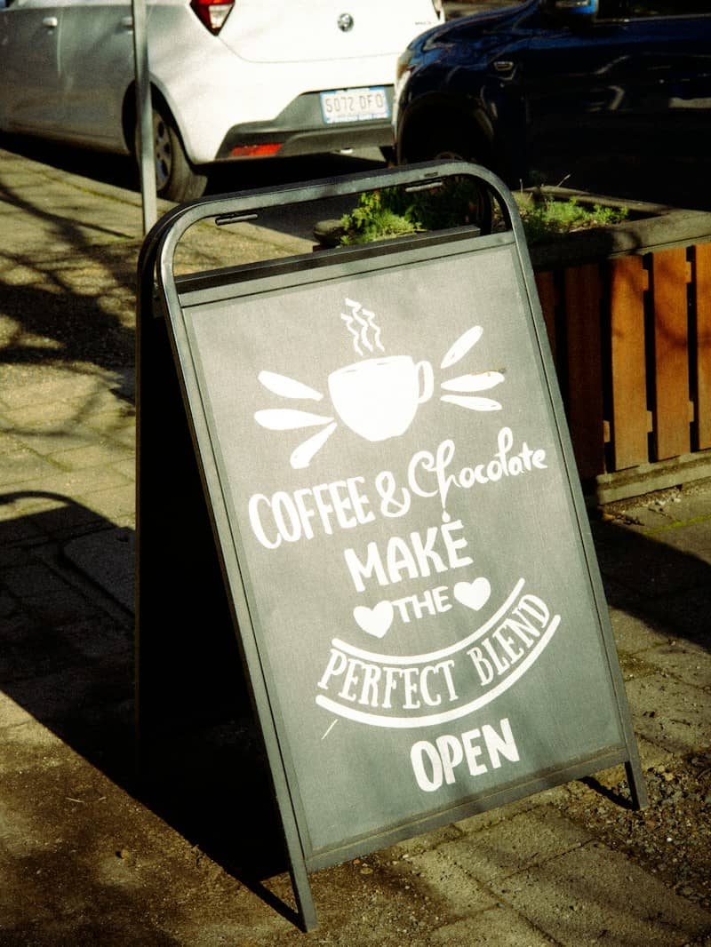 A black sandwich board sign with white text on a sidewalk