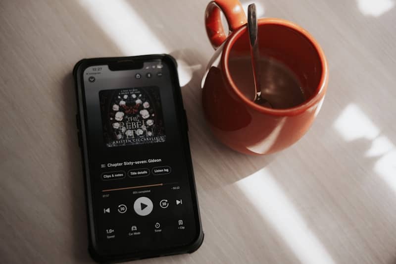 A smartphone displaying an audiobook app beside an orange mug on a wooden table