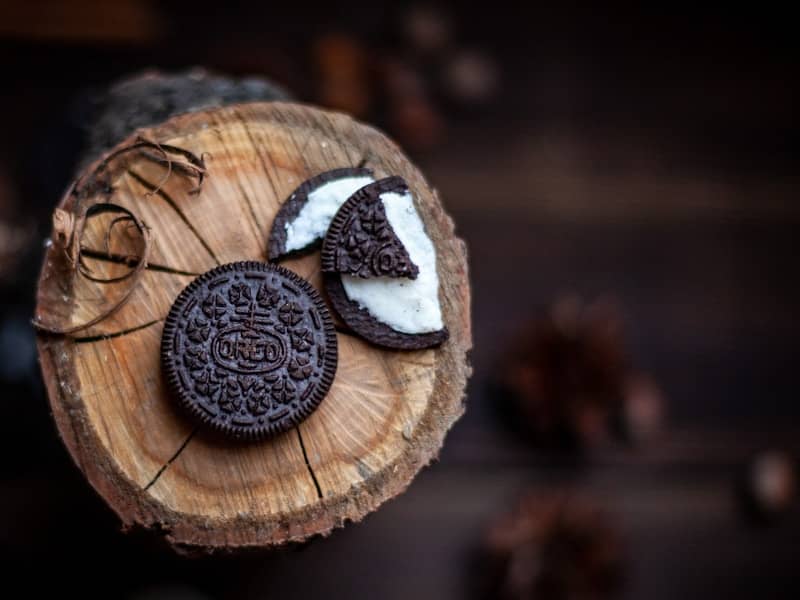 Two chocolate sandwich cookies with cream filling on wood.