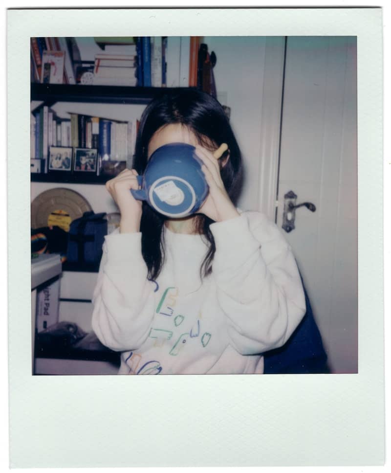 Woman drinking from a blue mug in front of bookshelf