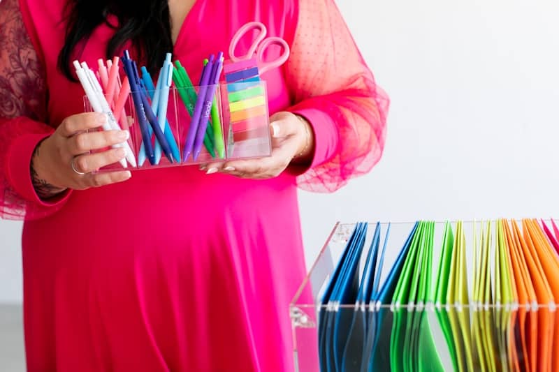 Woman in pink dress holding colorful pens and scissors.
