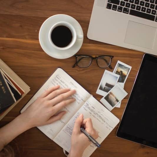 person holding ballpoint pen writing on notebook