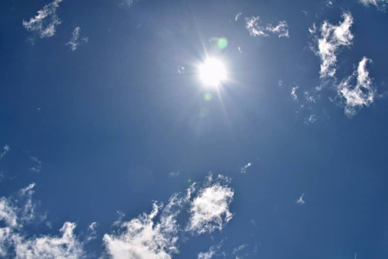 Bright sun in a blue sky with scattered white clouds.